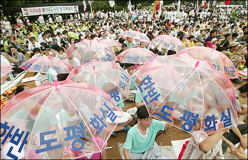 10일 오후 경기도 평택 대추리 대추초등학교에서 열린 '미군기지 확장 저지와 한반도 전쟁반대 7.10 평화대행진'에 참가한 시민단체 회원들이 평화실현 구호가 적힌 우산을 들고 있다. 